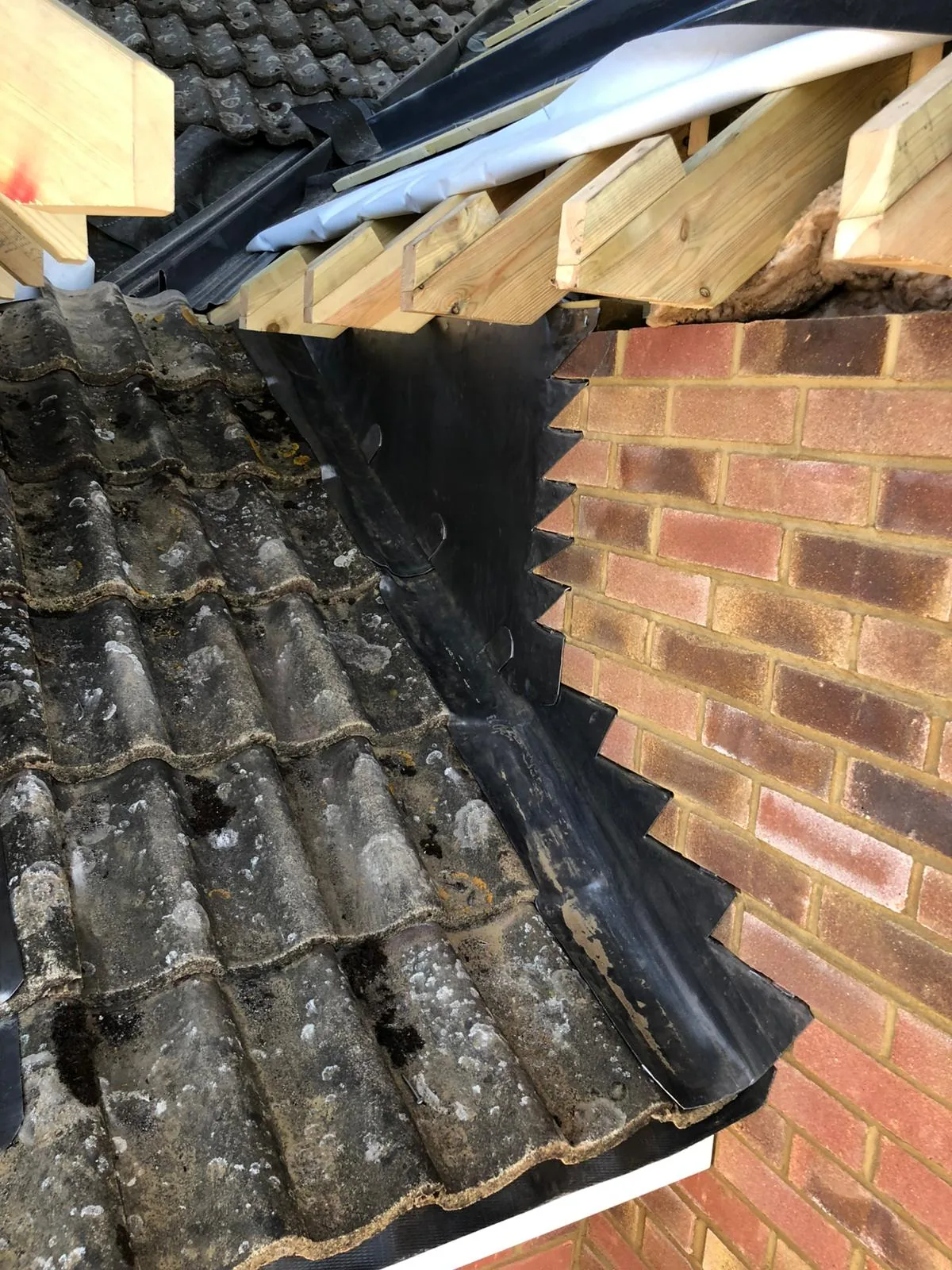 Close-up of lead flashings where old clay tiles meet a new brick gable